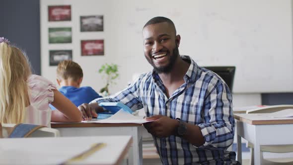 Video of happy african american male teacher helping pupils during lessons