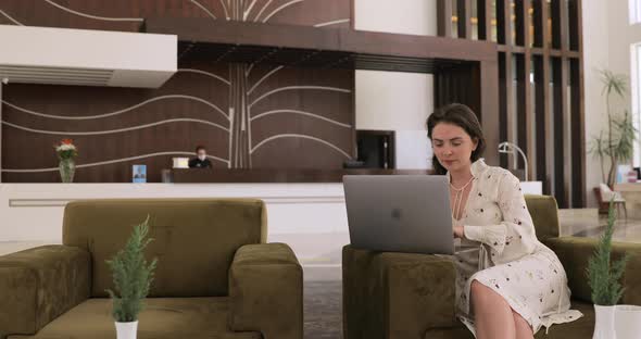 Attractive young woman is working with laptop in hotel lobby. Coronavirus travelling concept.