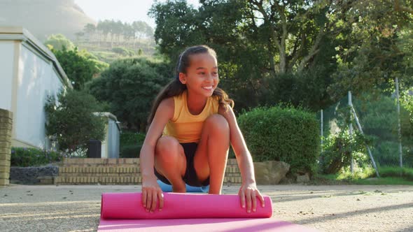 Mixed race schoolgirl rolling mat after yoga lesson outdoors