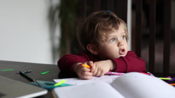 Little boy play with notebook, stickers and parents laptop at table at home alt