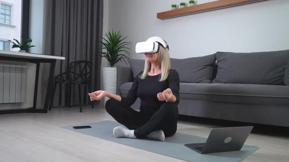 Cheerful Elderly Woman in Virtual Reality Glasses Meditates in the Living Room Modern Technology and