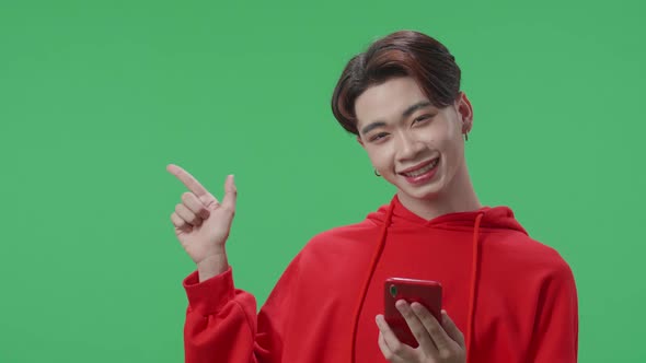 Transgender Male Flipping Through The Mobile Phone With A Smile Pointing To The Side On Green Screen