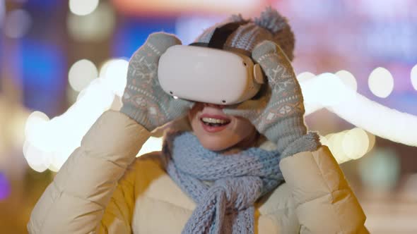 Excited Cheerful Young Woman Taking Off VR Headset Standing Outdoors on Winter Night in City