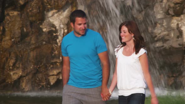 Couple walking in front of a waterfall in a garden.