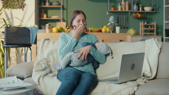 Mother Multitasking Holding a Baby Infant and Using Laptop at Home