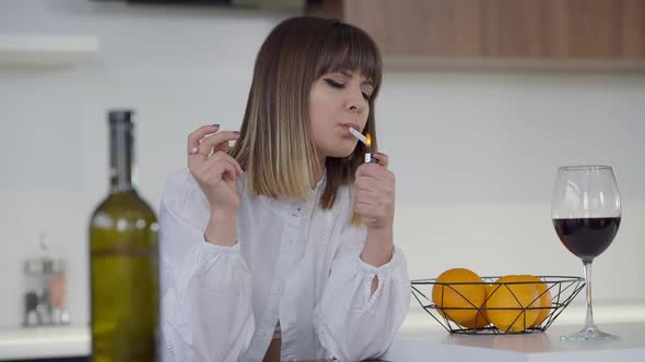 Medium Shot Portrait of Slim Beautiful Young Woman Lighting Cigarette Smoking in Kitchen at Home