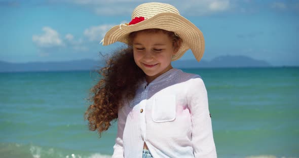 Portrait of a Funny Little Girl in a Hat a Smiling Child Looking at the Camera Stands on the Beach