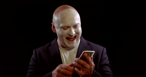 Crazy Man with White Greasepaint on Face Is Laughing and Typing on Smartphone