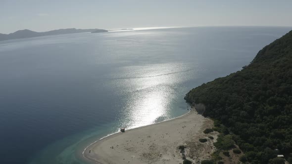 Aerial Drone Shot Zoom in Sun Reflection in the Ocean Sandy Beach Green Hill