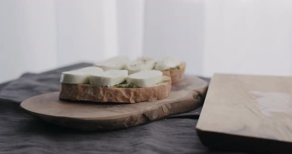 Slow Motion Man Making Ciabatta Bruschettas with Mozzarella and Pesto on Olive Board with Window on