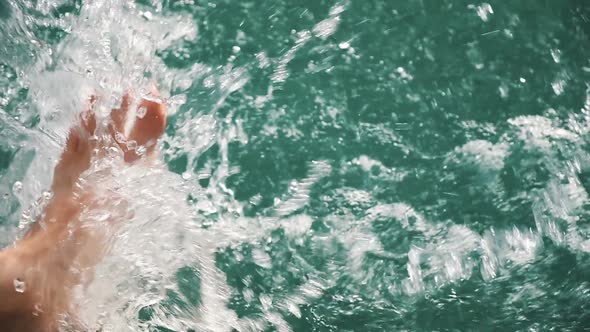 Women's Legs Floundering in Clear Water in Slow Motion, Flying Splashes of Water in the Sun