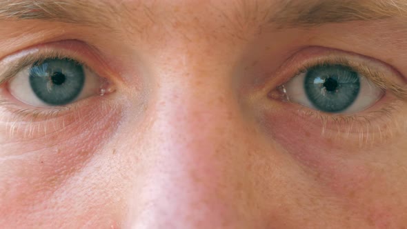 Close Up of Sad Male Blue Eyes Blinking and Looking Into Camera with Daylight. Portrait of Young