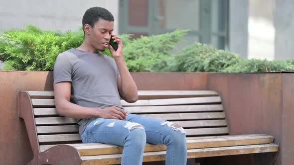 Upset Young African Man Angry on Smartphone on Bench 