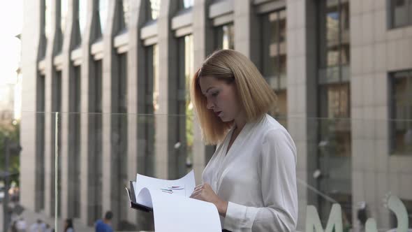 A young business woman is looking at documents for a new project outdoors. Business growth charts.