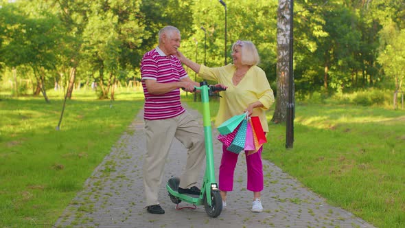 Elderly Stylish Couple Grandmother Grandfather After Shopping with Bags Using Scooter for Riding