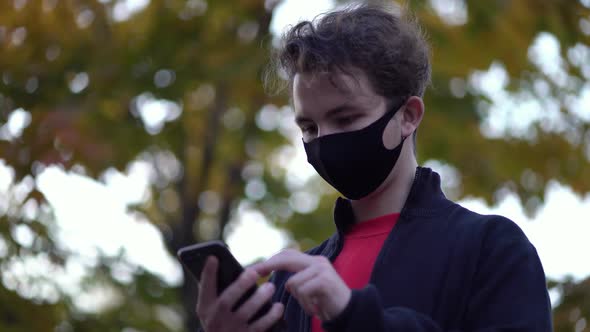 Portrait Boy in Protective Medical Mask Walks Down To the Street Uses Phone Texts Scrolls Surfs the