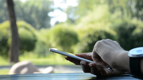 Hands of Woman Typing on Smartphone in Sunny Day in Summer