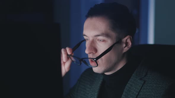 Afraid and Shocked Man Looking at Monitor Screen Takes Off Glasses and Cover His Mouth with His Hand