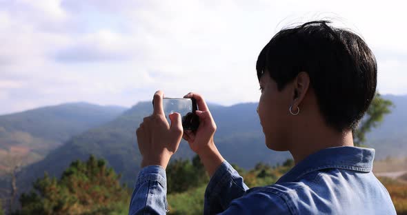 Young Asian traveler taking video with smart phone on top of the mountain.