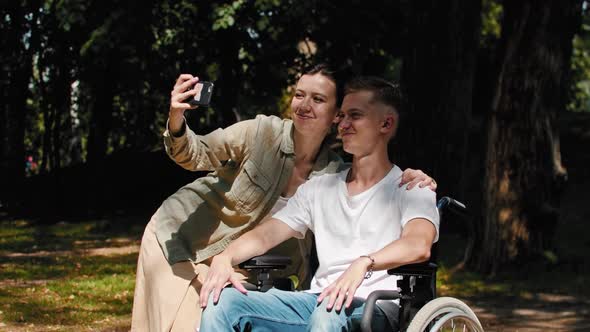 Man in a Wheelchair and His Girlfriend Spending Time at the Summer Park and Taking a Selfie Together