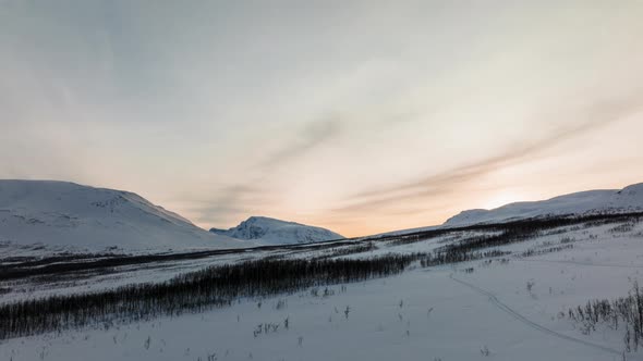 Dynamic aerial shot of a landscape full of snow at orange sunset. Acrobatic drone