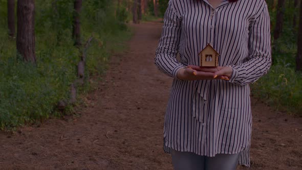 Close Up of Body Part of Woman with Small Wooden House in Hands Standing in Forest