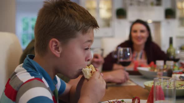 Smiling caucasian son eating at table during family meal, parents in background
