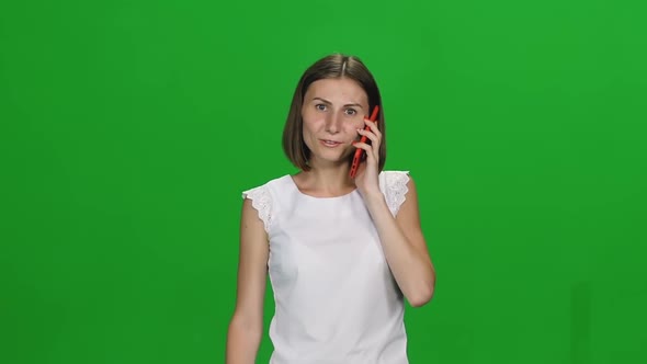 Portrait of Young Woman Is Calmly Walking and Talking on Mobile Phone on Green Screen. Front View