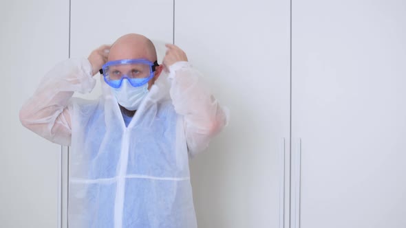 A Tired Doctor in the Locker Room Takes Off His Protective Clothing After His Shift in the