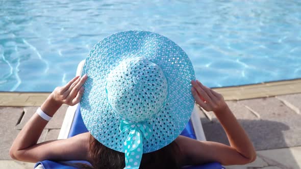 Happy Young Woman in Blue Hat Lies Down on Lounger in Hotel