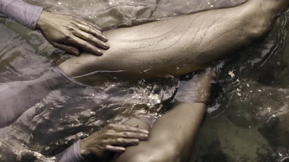 Young Graceful Woman Is Stroking Her Legs with Skin Covered Gold Dye Lying in Water