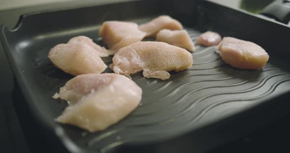 Raw pieces of chicken fillet are placed in a hot pan and fried