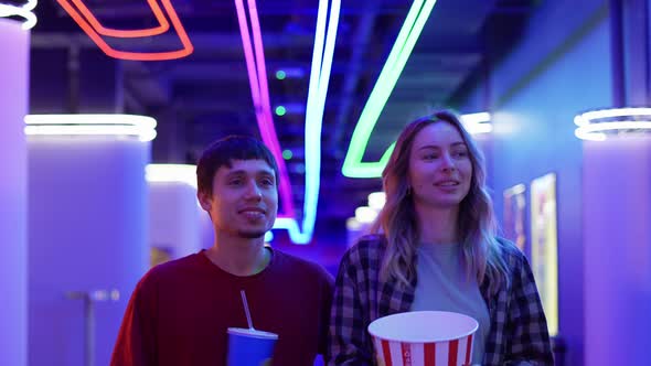 Happy Young Woman and Man Walking with Bucket of Popcorn and Drink Chatting at Cinema