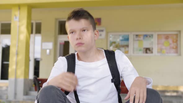 A Caucasian Teenage Boy Stretches As He Sits in Front of School  Closeup