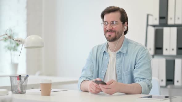 Young Man Listening to Music on Smartphone at Work