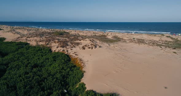 Drone flies low over dunes overlooking wild beach and toursit enjoying of summer