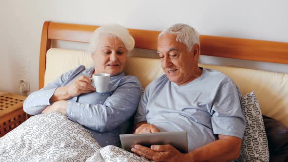 Senior woman using digital tablet and man having cup of coffee