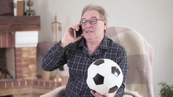 Portrait of Positive Elderly Grey-haired Man Talking on the Phone and Holding Football Ball