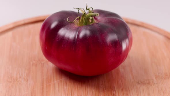 Close up view of ripe black variety of tomato on wooden cutting board isolated in background.