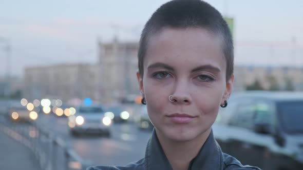 Young Attractive Woman with Shaved Hair Against Highway with Traffic at Sunset.