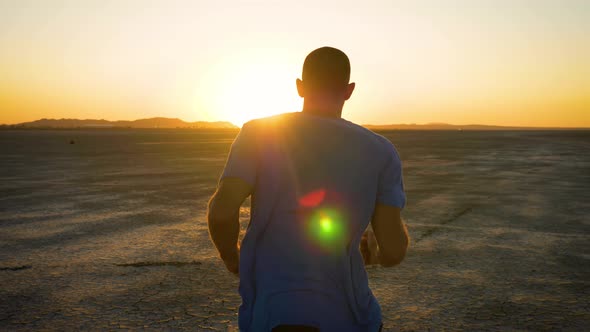 Athletic man working out with battle ropes on a dry lake at sunset