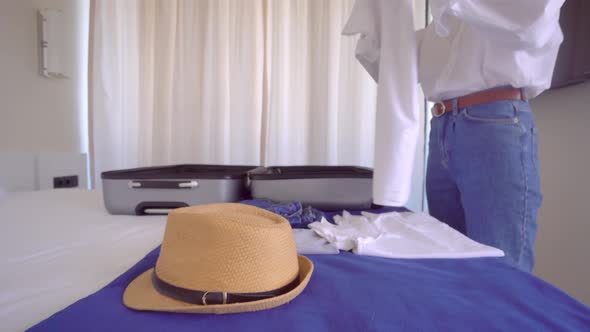 A young beautiful woman in a white shirt collects things in a suitcase