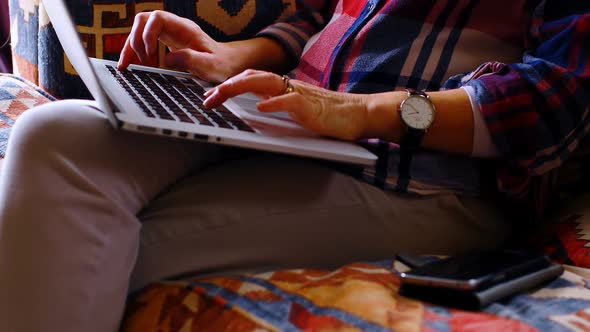 Woman talking on mobile phone while using laptop at home 4k