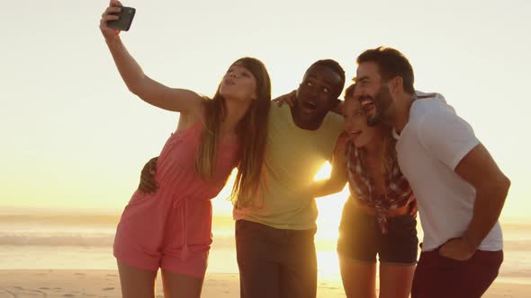 Young adult friends taking seflies on the beach at sunset 4k