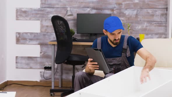 Male Worker in Overalls Wearing a Cap Reading Furniture Assembly