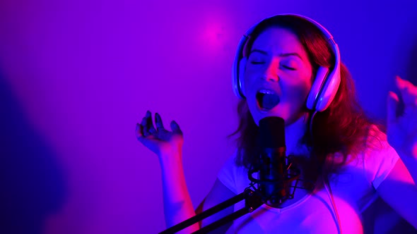 Caucasian Woman in Headphones Sings Into a Microphone in Neon Light