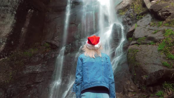 girl in Santa Claus hat stands on waterfall on Christmas Day. Enjoying nature