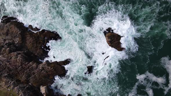 Aerial - Turbulent water as waves crashes into rocky coastline, top-down view