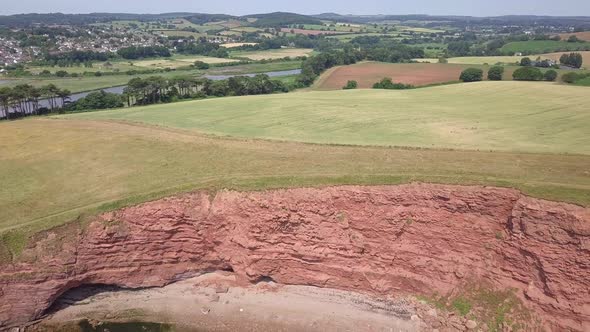 4K, Red sandstone bay cliffs and countryside landscape at UK coastal town, AERIAL PULL BACK