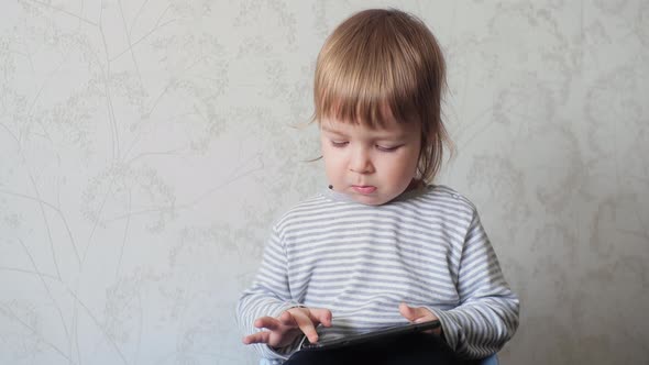 A Small Child Holding a Digital Tablet and Tapping the Screen of an Electronic Device